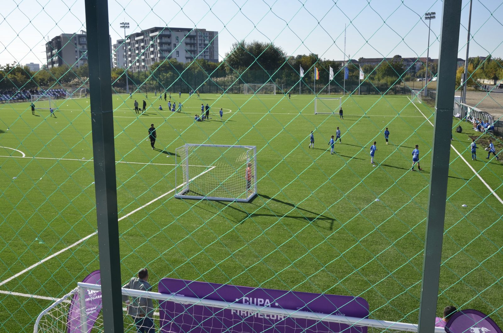 Copii jucând fotbal pe terenul sintetic, văzuți de pe terasă