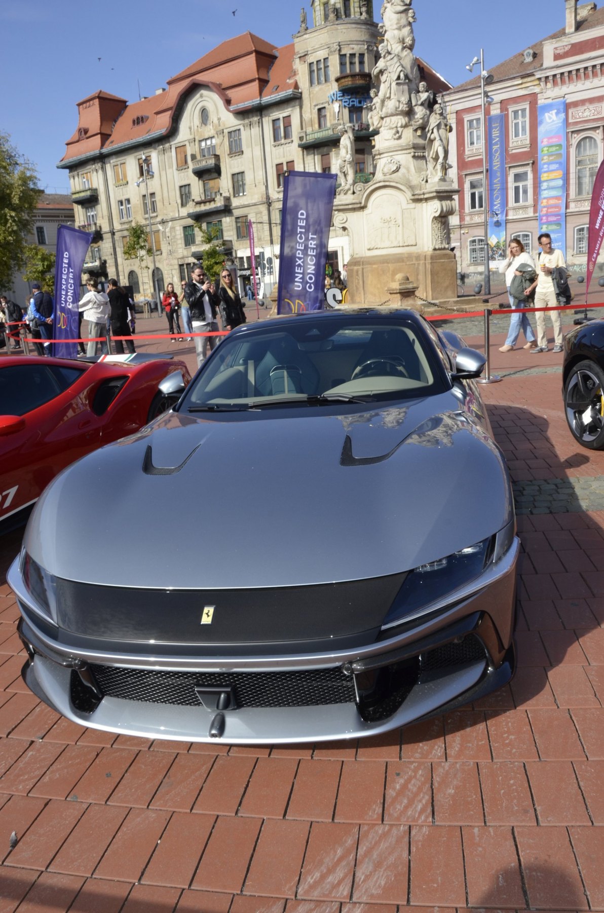 Ferrari gri, văzut din față, cu vizitatori în fundal