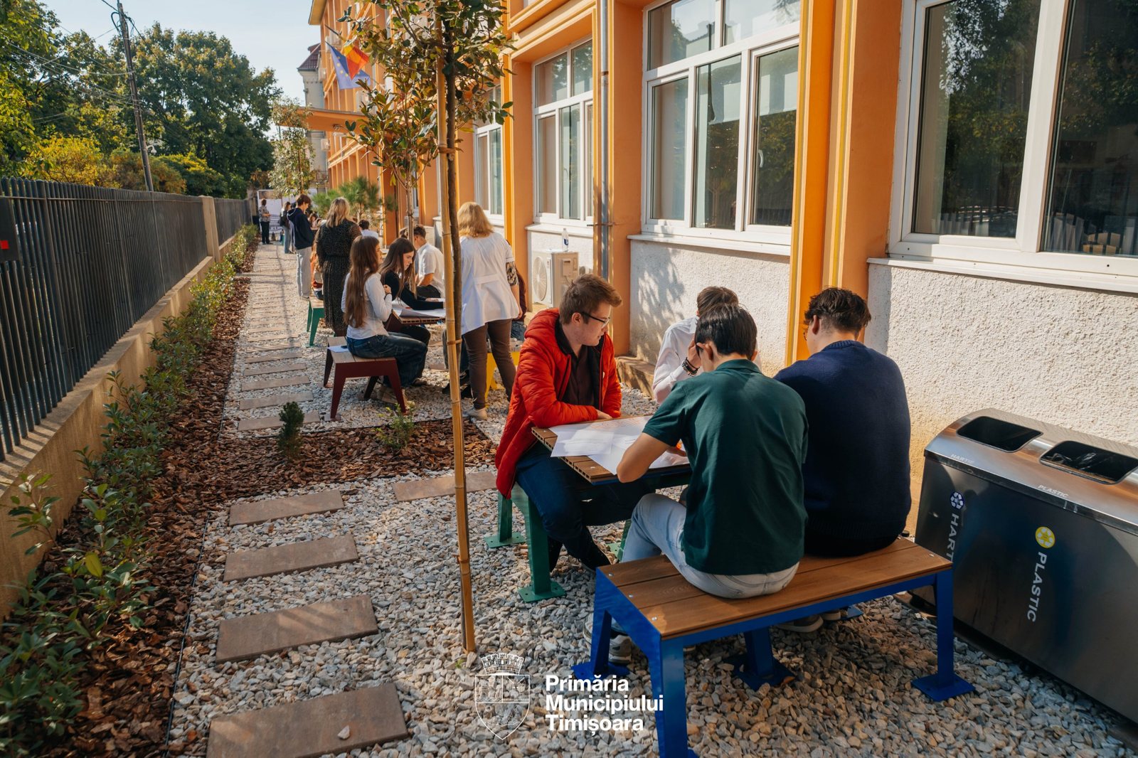 Elevi lucrând pe echipe la mese colorate în curtea liceului