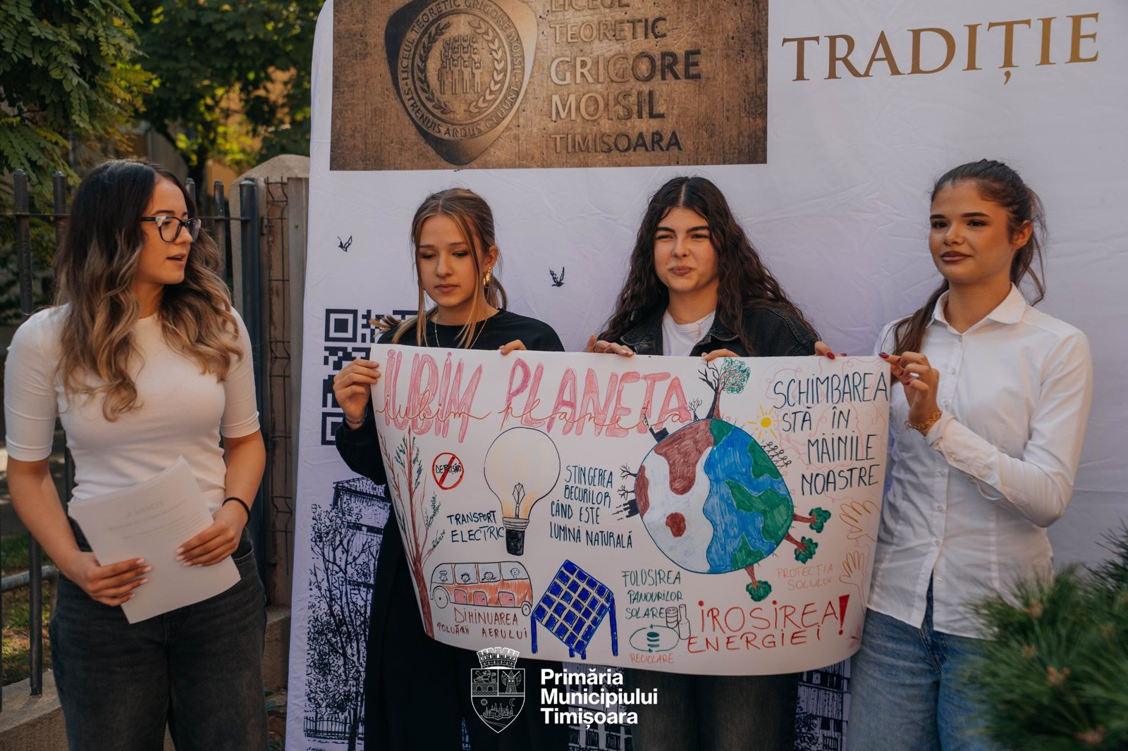 Eleve prezentând planșa Iubim planeta în fața bannerului Liceului Teoretic Grigore Moisil