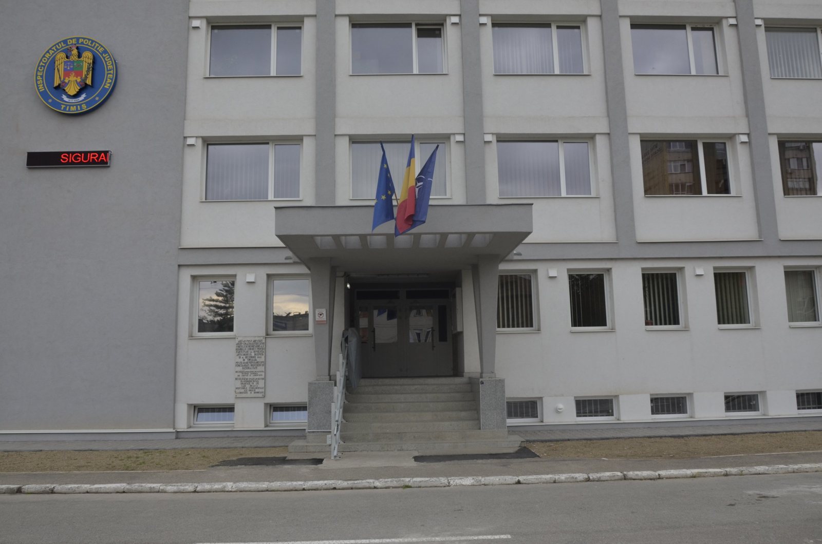 Intrarea principală în sediul IPJ Timiș, cu emblema instituției și drapelele României, UE și NATO