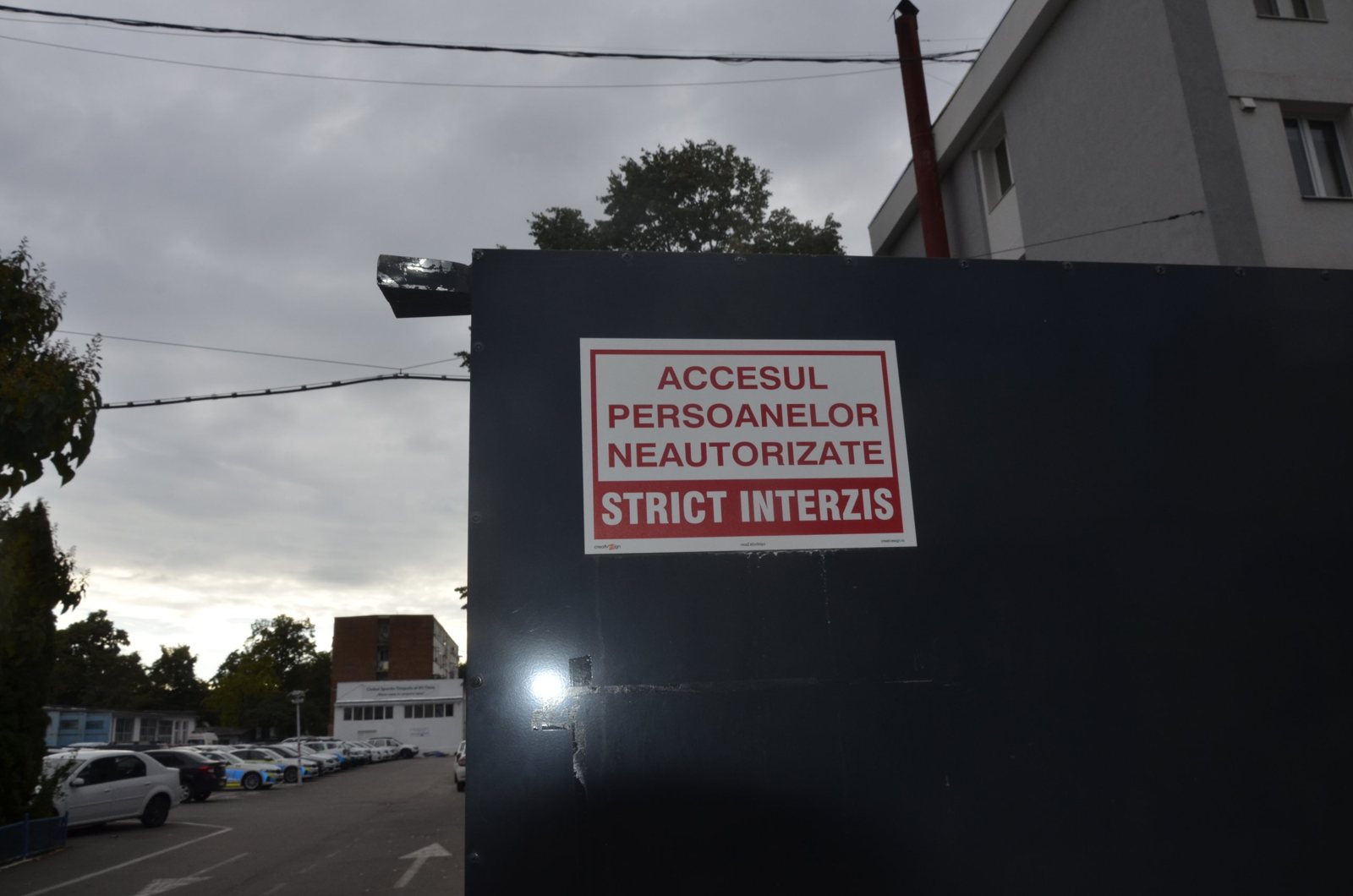Panou cu inscripția Accesul persoanelor neautorizate strict interzis pe poarta IPJ Timiș, cu parcarea de mașini de poliție în spate