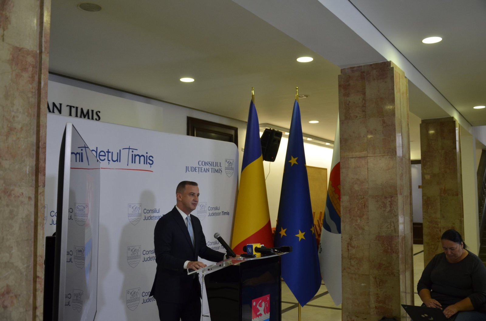Alfred Simonis vorbind, cu drapelele României și Uniunii Europene în spate