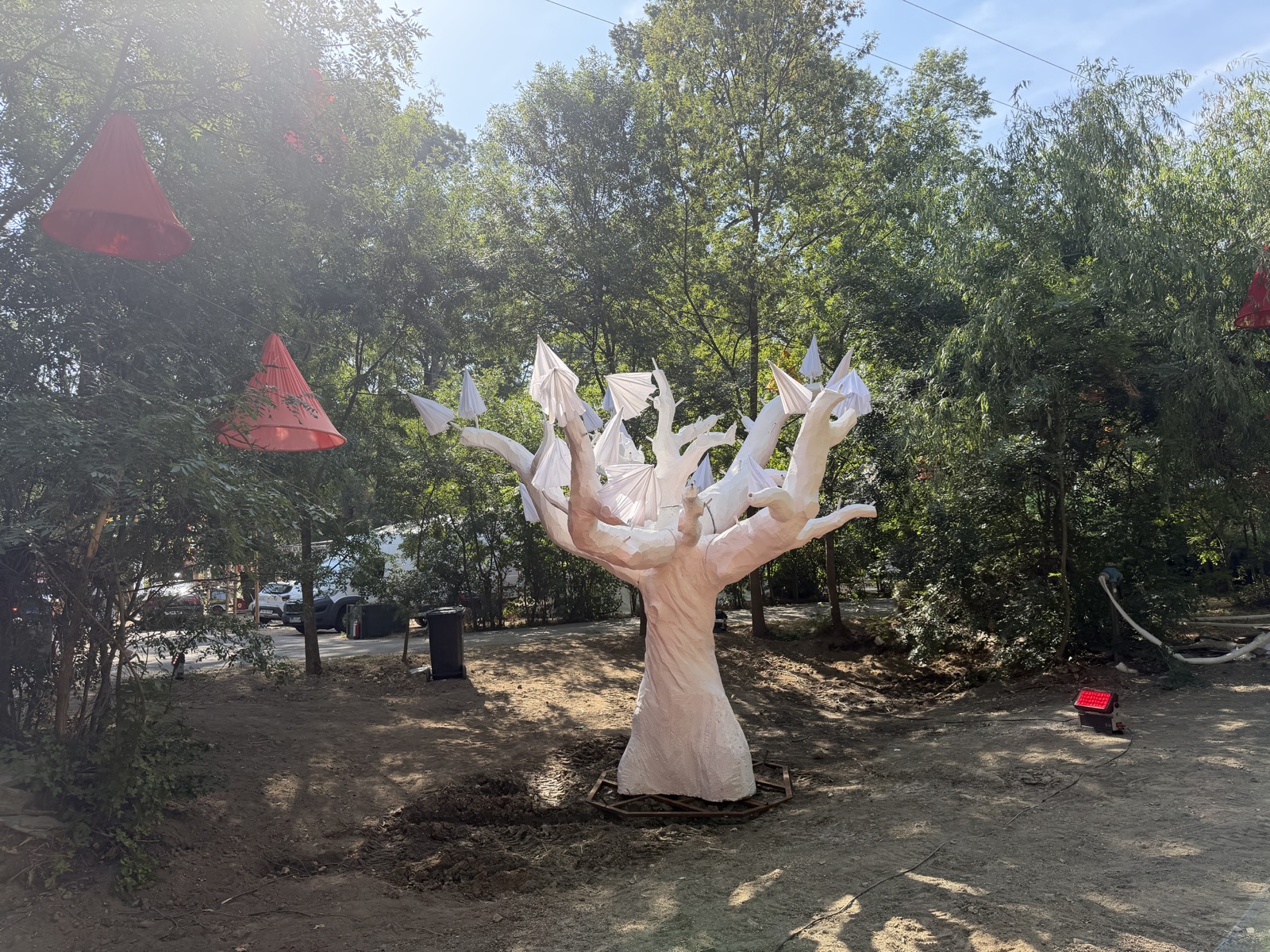Instalație artistică în formă de copac, cu abajururi roșii suspendate în apropiere
