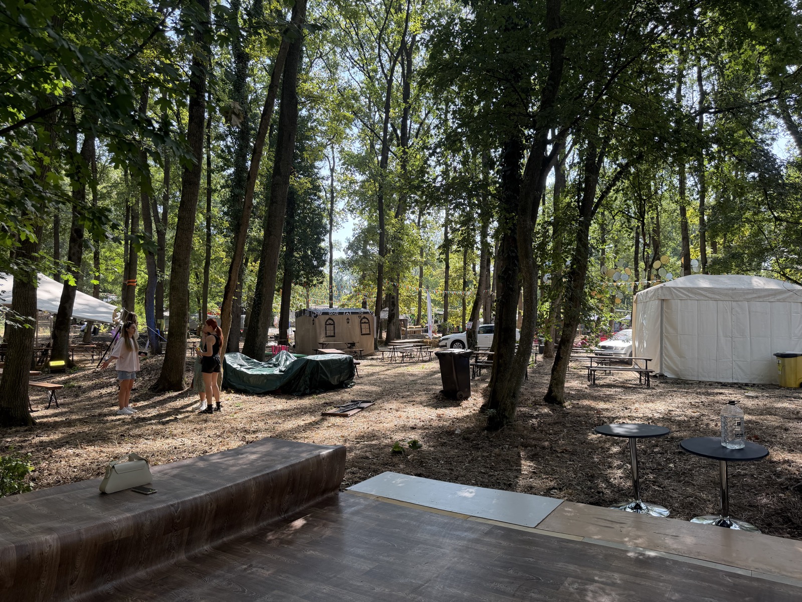Zonă de relaxare din pădure, cu corturi albe, mese și vizitatori