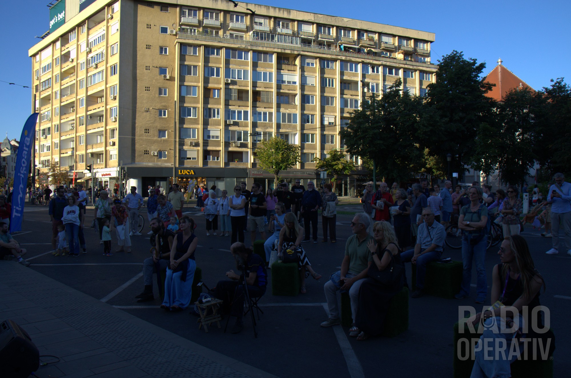 Public așezat pe cuburi de iarbă artificială, pe carosabil, urmărind concertul