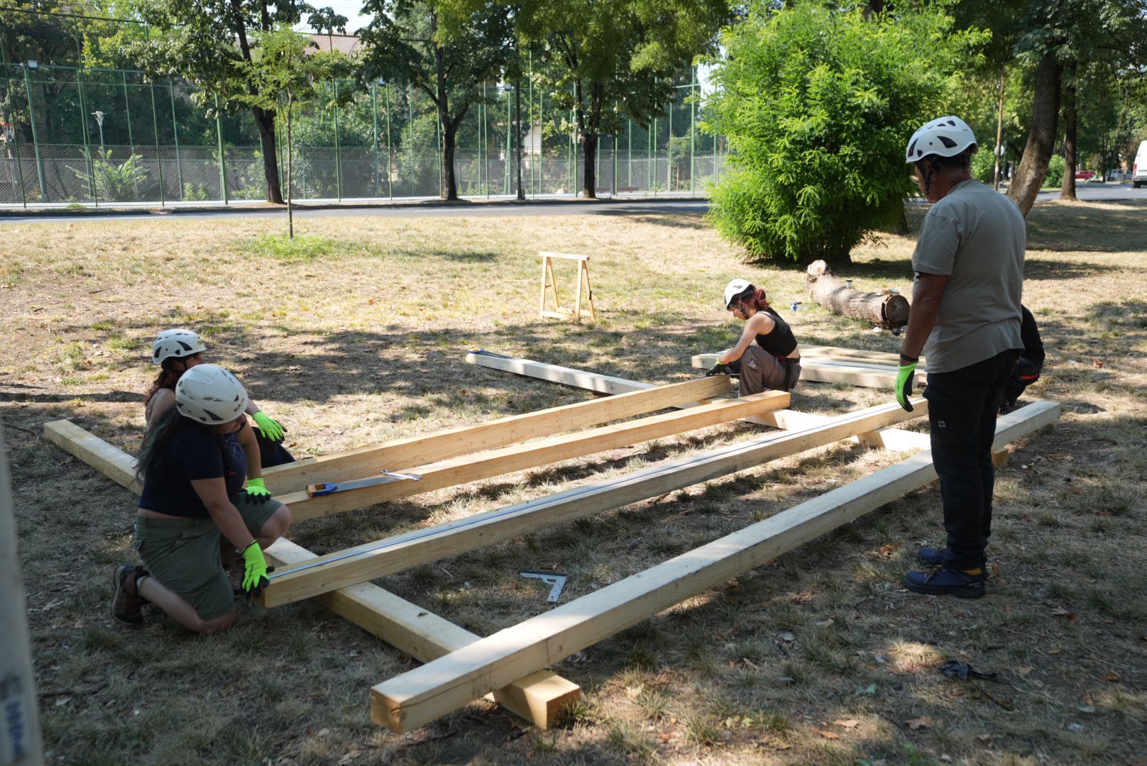 Voluntari asamblează pe iarbă o structură din grinzi de lemn pentru șarpantă