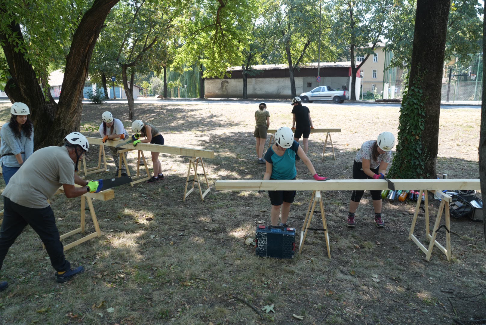 Voluntarii taie grinzi de lemn cu fierăstrăul, sub coordonarea specialiștilor